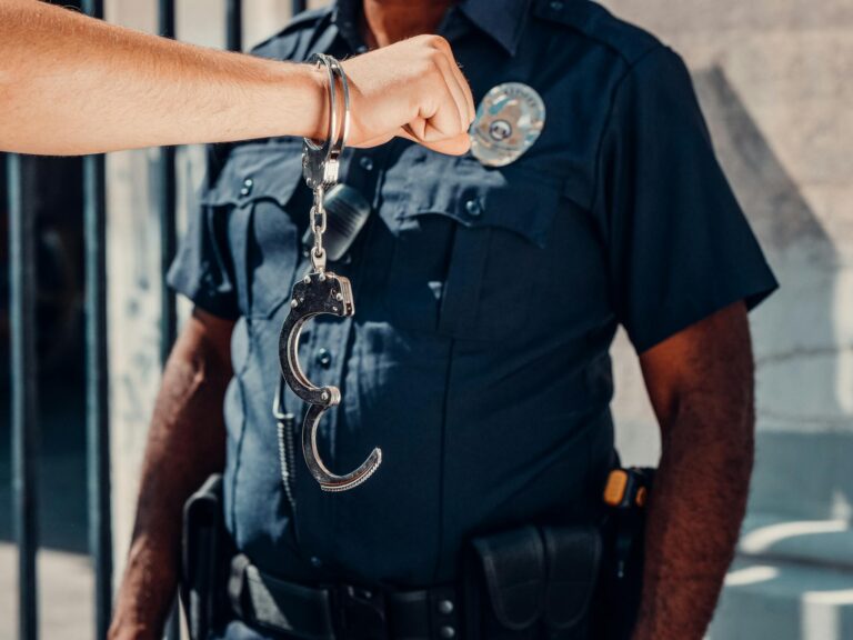 A police officer in uniform holds open handcuffs outdoors, clear authority symbol.
