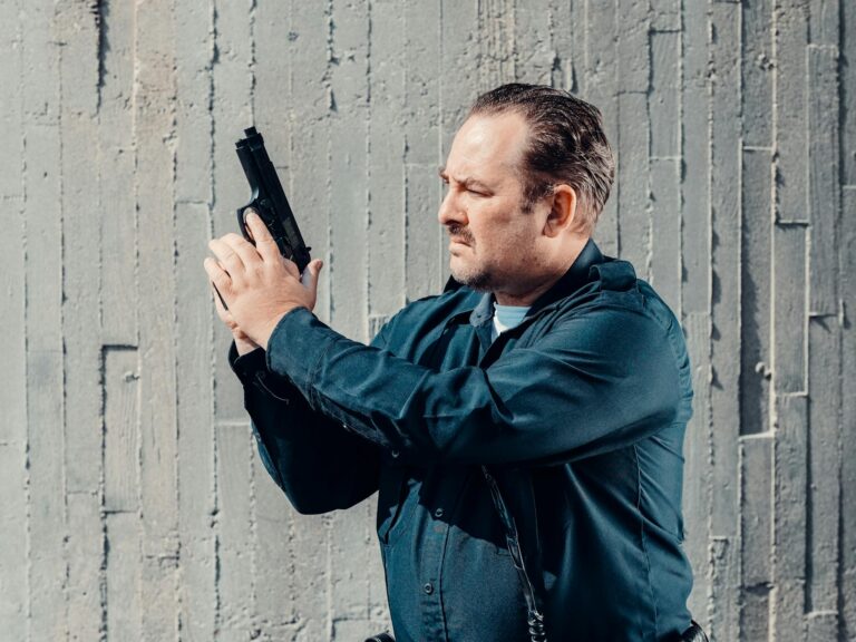 Officer standing against a concrete wall, securing a firearm, representing law enforcement and safety.